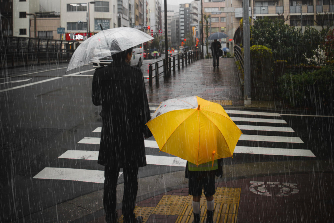 Bărbat și copil cu umbrele în ploaie