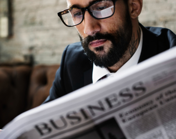 Un bărbat cu barbă și ochelari citește un ziar
